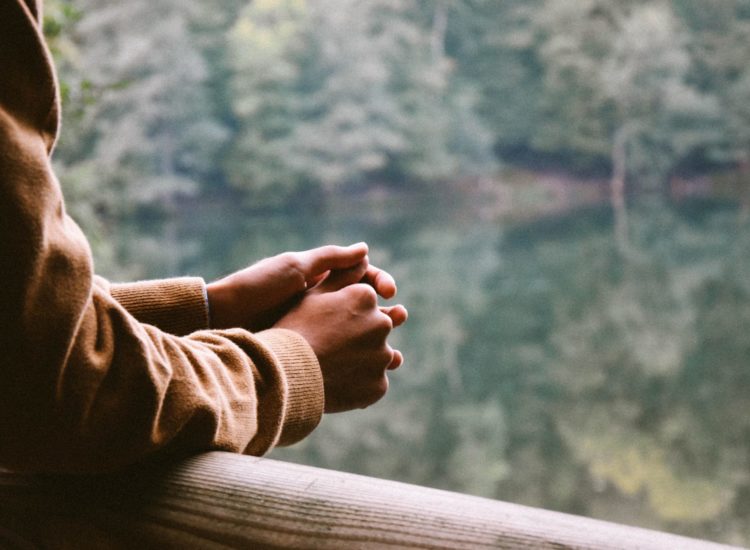 A close up of someone holding their hands together overlooking a balcony into the forest.
